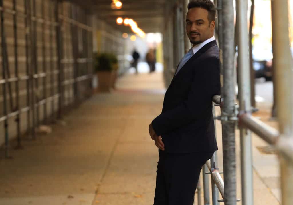 A man in a suit leaning against a fence representing an employment lawyer.
