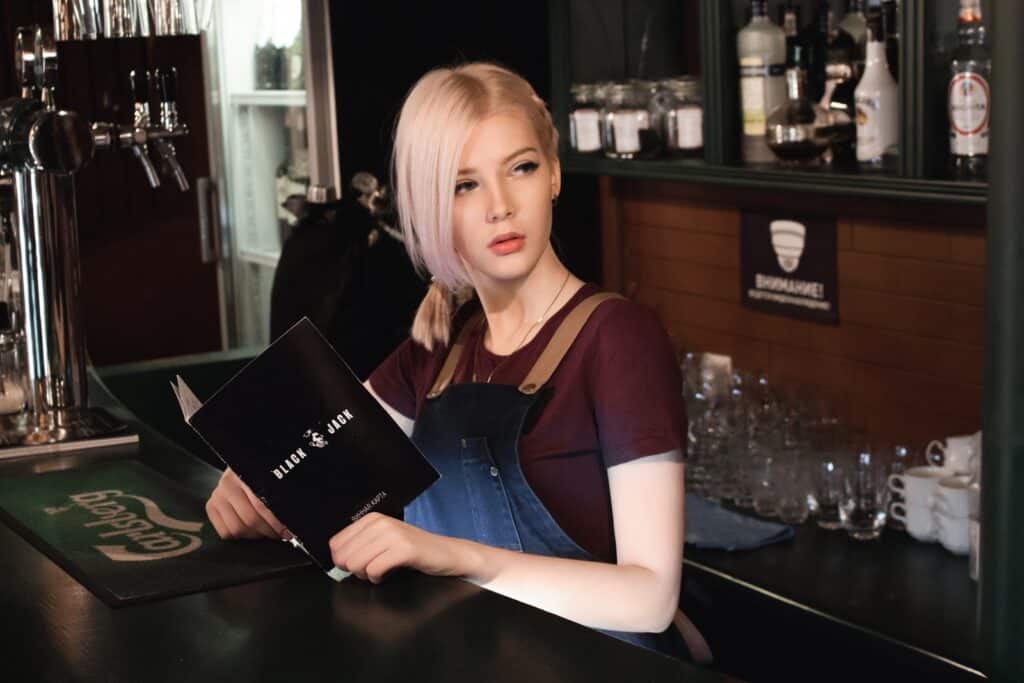 A woman standing behind a bar holding a book.