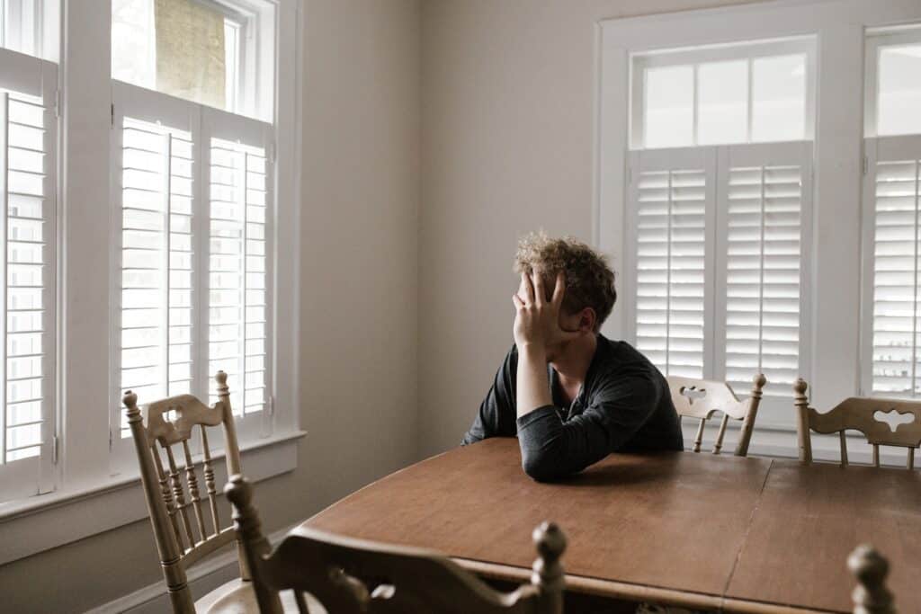 A man sitting at a table in front of shuttered windows.