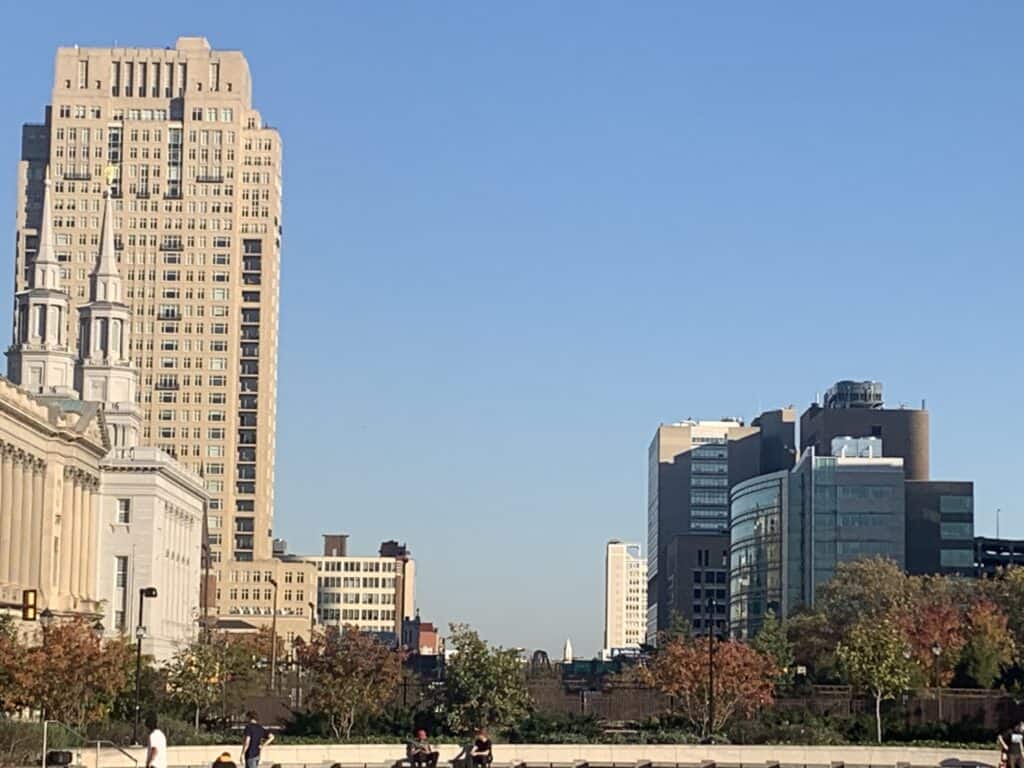 A group of people walking in a park near tall buildings is observed by an employment lawyer.