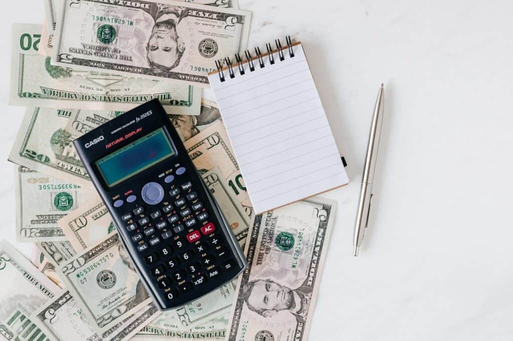 A calculator sits on top of a pile of money and a notepad.