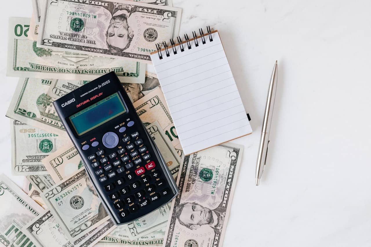 A calculator sits on top of a pile of money and a notepad.