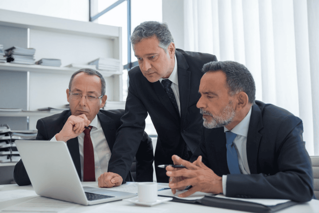 Three businessmen consulting with an employment lawyer while looking at a laptop in an office.