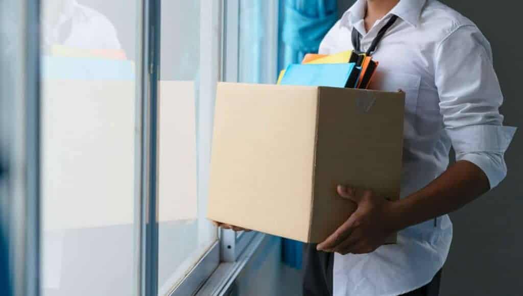 A man holding a box of papers in front of a window.