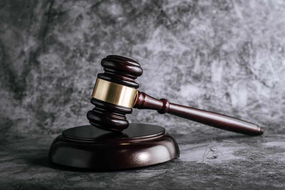 A wooden gavel rests on a matching sound block against a gray marbled background.