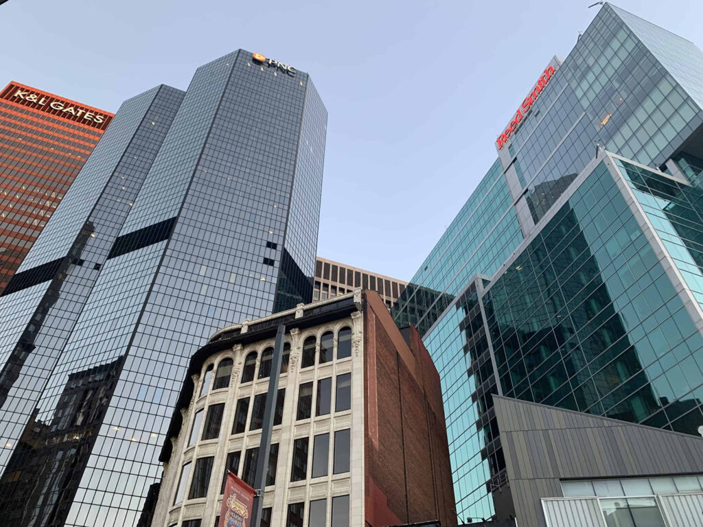 Several modern glass skyscrapers and an older brick building stand close together under a clear sky, with company names and "Homepage" banners visible on some towers.