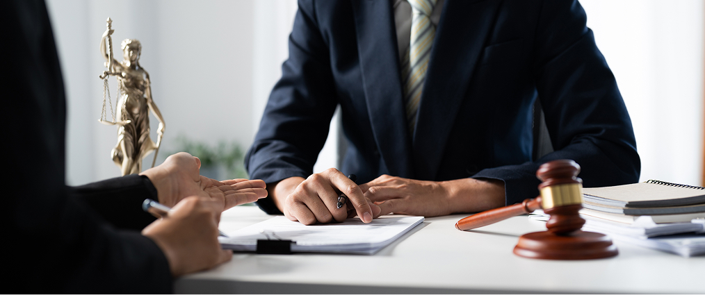 Two people in business attire sit at a desk with legal documents, a gavel, and a Lady Justice statue, engaged in discussion—an image perfect for your law firm's homepage.