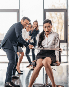 A man in business attire pulls a rope tied around a woman seated on an office chair, while two colleagues watch and react in the background, highlighting subtle workplace race discrimination dynamics.