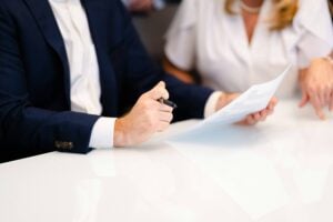 Two people sit at a table; one holds a pen and a document, while the other gestures toward the paper. Their faces are not visible, suggesting a confidential discussion—perhaps with an employment attorney Philadelphia residents trust for workplace concerns.
