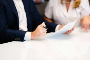 Two people in business attire sit at a table, with one person holding a pen and reviewing a document while the other points at the paper—illustrating why it’s essential to Hire an Employment Attorney for navigating important workplace agreements.