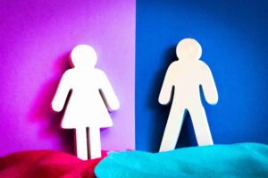 Two white symbols, one for a woman and one for a man, stand against a split pink and blue background with red and blue fabric at the bottom—an image that reflects issues addressed when seeking how to find a gender discrimination lawyer near me in New Jersey.