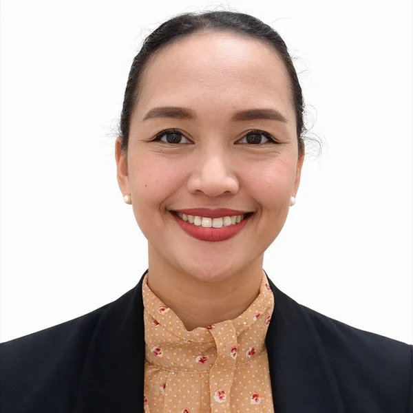 A woman with dark hair tied back, wearing a black blazer and a beige patterned blouse, smiles at the camera against a plain white background. Karen Montero exudes confidence and warmth in this professional portrait.