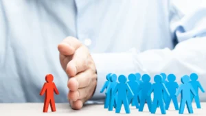 A hand separates a single red figure from a group of blue figures, symbolizing exclusion or segregation—reflecting issues like pregnancy discrimination that New Jersey lawyers work to combat.