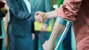 A person using crutches in the foreground while two people in business attire shake hands in the background, highlighting the importance of Philadelphia Disability Discrimination Lawyers in supporting workplace equality.