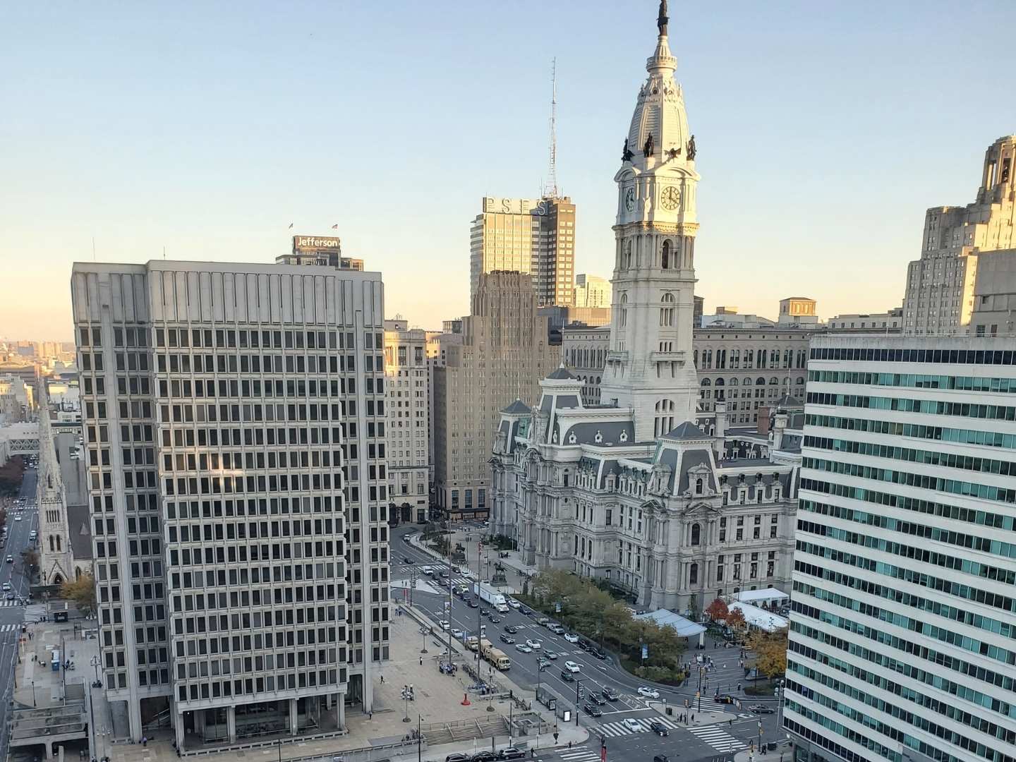 Aerial view of Philadelphia City Hall surrounded by tall office buildings, including The Lacy Employment Law Firm, with streets and cars visible below on a clear day.