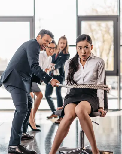 A man in business attire pulls a rope tied around a woman seated on an office chair, while two colleagues watch and react in the background, highlighting subtle workplace race discrimination dynamics.
