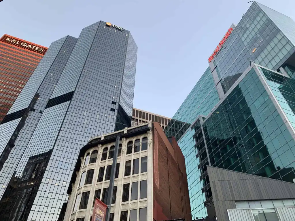 Tall modern glass office buildings tower over an older brick building in an urban cityscape under a clear sky, with The Lacy Employment Law Firm occupying a prominent space among the city’s bustling legal hubs.