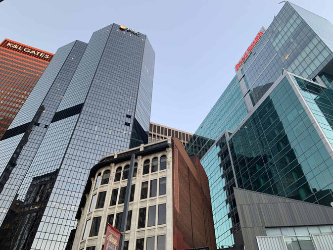 Several modern glass skyscrapers tower over an older, shorter brick building in an urban cityscape under a clear sky, with The Lacy Employment Law Firm prominently situated among the downtown offices.