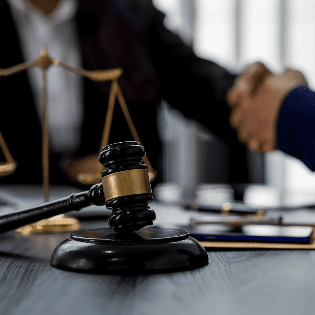 A judge’s gavel and scales of justice are on a table in the foreground, while two people shake hands in the blurred background, reflecting a successful resolution with Lacy Employment Law Firm.