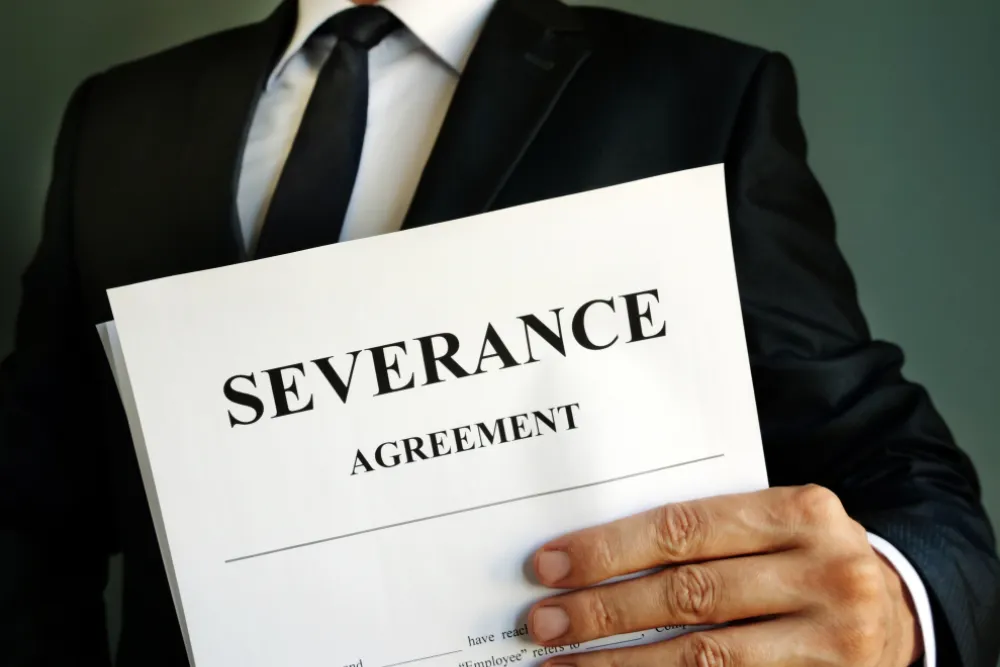 A person in a suit holds a document labeled "Severance Agreement," ready to discuss the terms of the severance agreement with their employer.