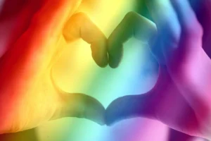 Two hands form a heart shape against a bright rainbow-colored background, symbolizing love, LGBTQ+ pride, and the vital support of an LGBT discrimination lawyer in championing equality for all.