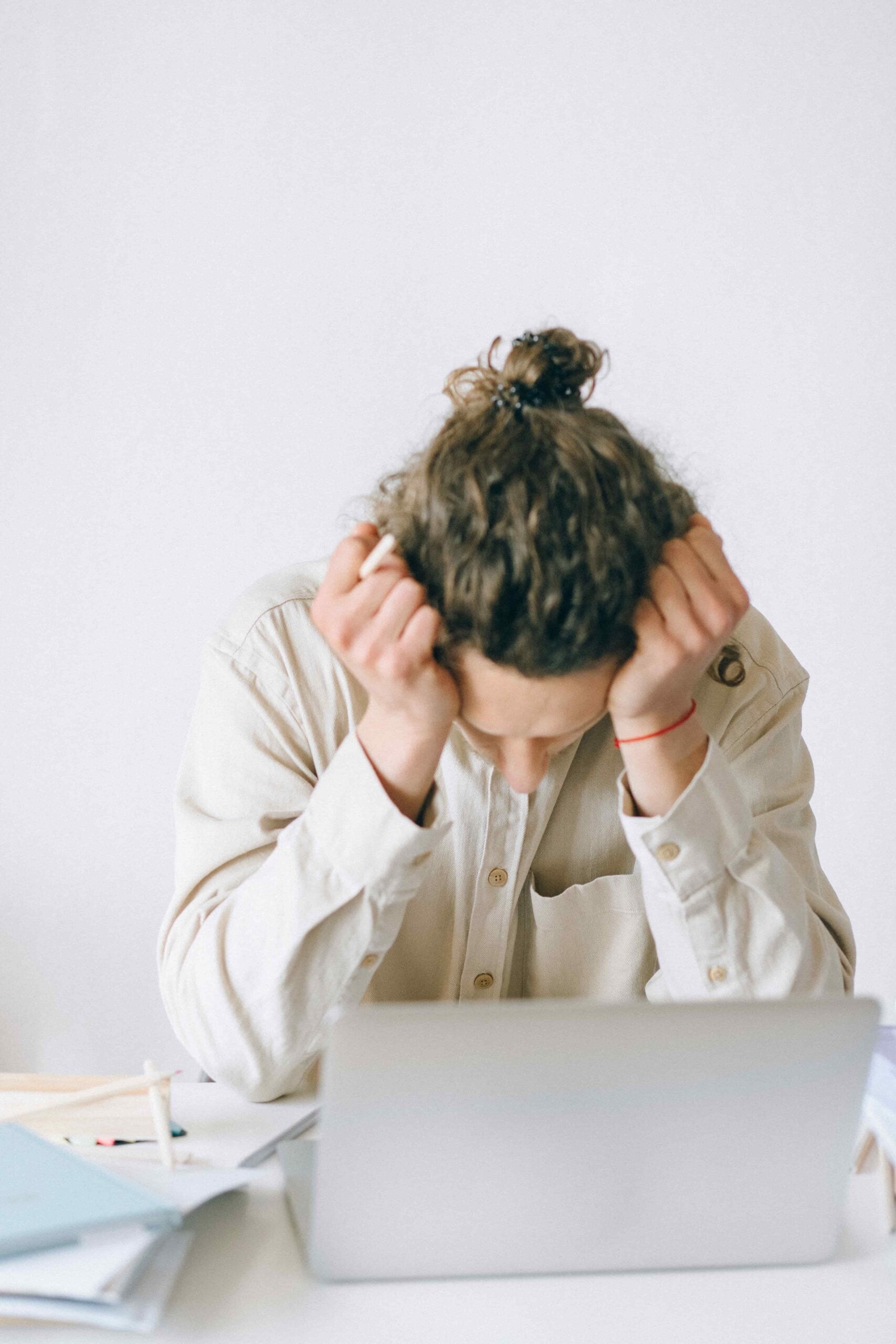 Person with head down and hands on forehead sits at a desk with a laptop and papers, appearing stressed or frustrated—possibly overwhelmed by concerns about family leave or medical leave.