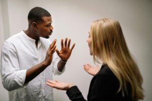 A man and a woman having an animated conversation indoors about how to choose a workplace harassment lawyer in New Jersey; the man gestures with his hands while the woman listens and responds.