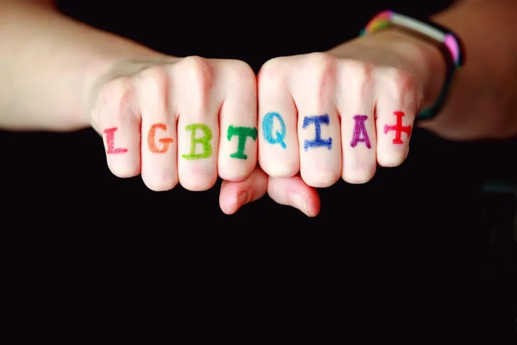 Two fists are shown with the letters “LGBTQIA+” written in colorful marker across the knuckles, against a black background—a powerful visual statement reflecting the fight for equality championed by every LGBT discrimination lawyer.