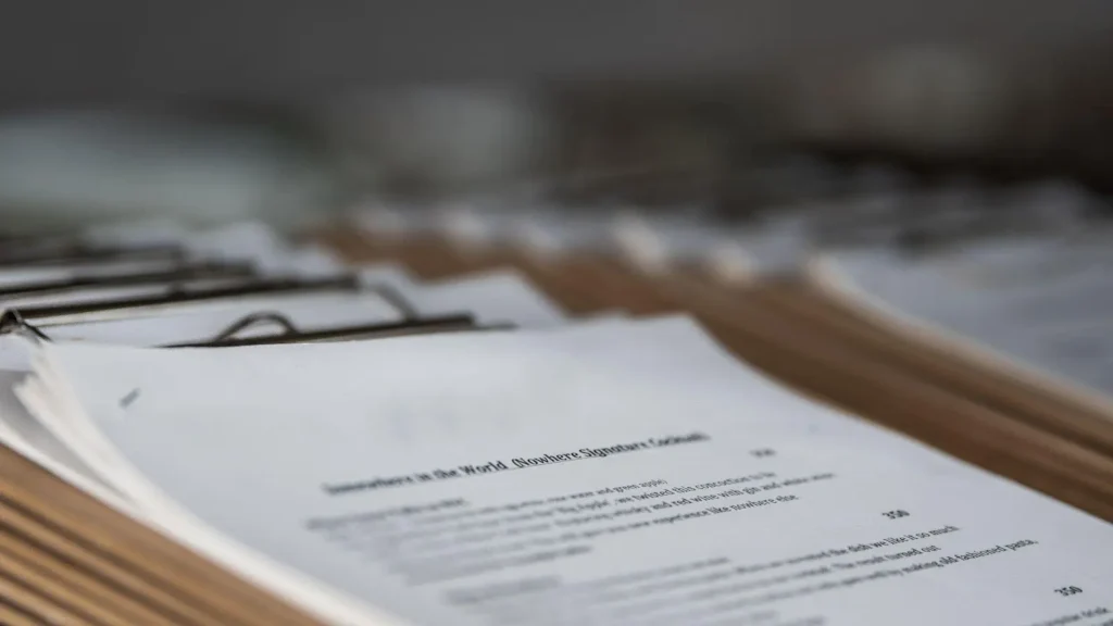 Stack of clipboards holding printed documents arranged in a row, with the text on the front page partially visible and out of focus in the background.