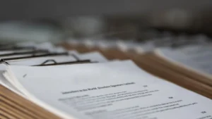 Stack of clipboards holding printed documents arranged in a row, with the text on the front page partially visible and out of focus in the background.
