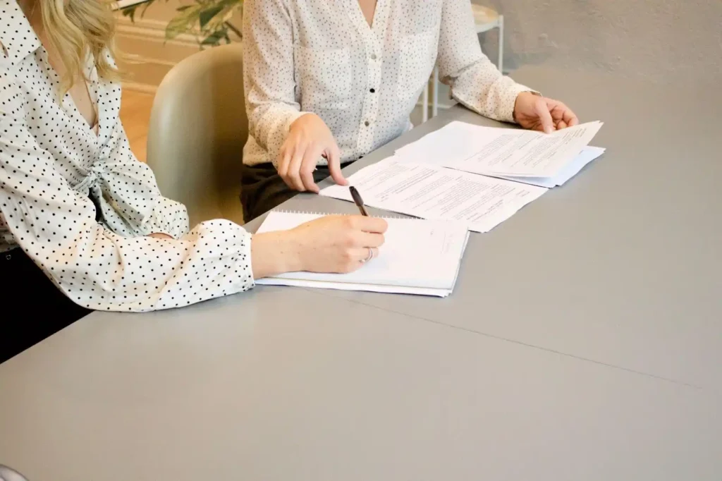 Two people in polka dot shirts sit at a table reviewing and discussing maternity documents together, with pens and papers in hand.