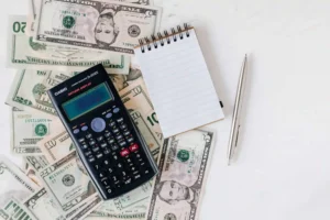 A scientific calculator, a blank notepad, and a pen are placed on top of assorted US dollar bills on a white surface, evoking the meticulous calculations often involved in understanding Philadelphia Minimum Wage Laws.