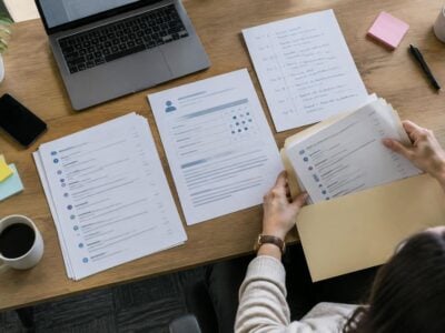 Person reviews resumes at a desk with a laptop, coffee, and handwritten notes—searching for retaliation evidence among printed documents to help prove retaliation in the workplace.